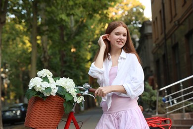 Photo of Beautiful teenage girl near bicycle with basket of flowers on city street