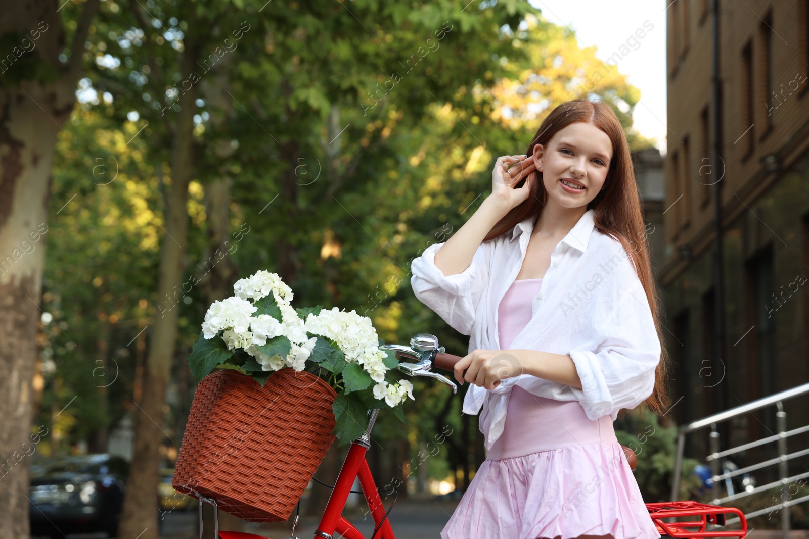 Beautiful teenage girl near bicycle with basket of flowers on city street Photo of Beautiful teenage girl near bicycle with basket of flowers on city street
