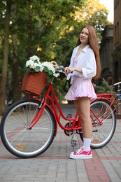 Photo of Beautiful teenage girl near bicycle with basket of flowers on city street