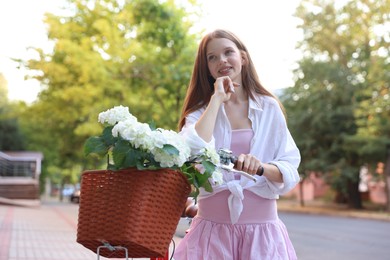 Photo of Beautiful teenage girl near bicycle with basket of flowers on city street
