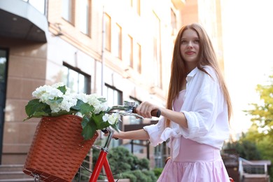 Photo of Beautiful teenage girl near bicycle with basket of flowers on city street