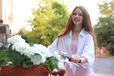 Photo of Beautiful teenage girl near bicycle with basket of flowers on city street