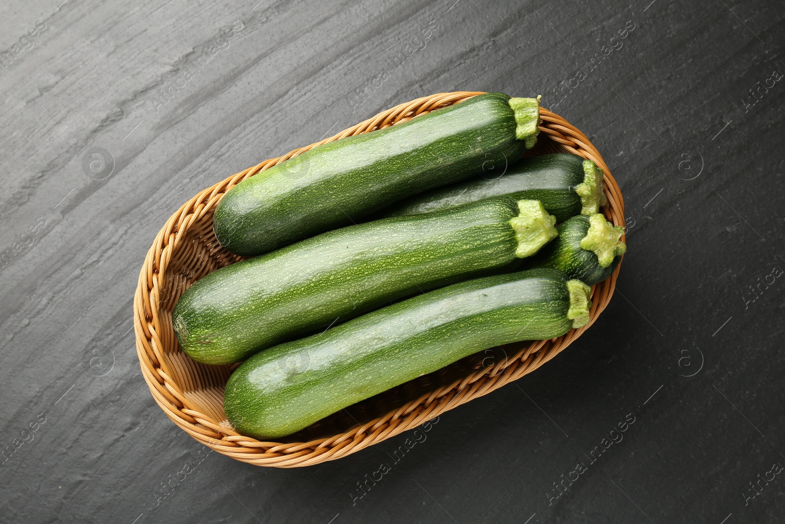Fresh ripe zucchinis in wicker basket on black table, top view Photo of Fresh ripe zucchinis in wicker basket on black table, top view