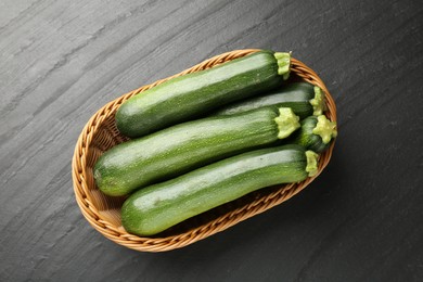 Photo of Fresh ripe zucchinis in wicker basket on black table, top view