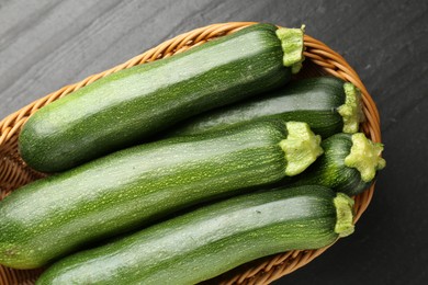 Photo of Fresh ripe zucchinis in wicker basket on black table, top view