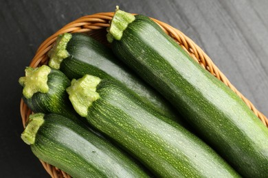 Photo of Fresh ripe zucchinis in wicker basket on black table, top view