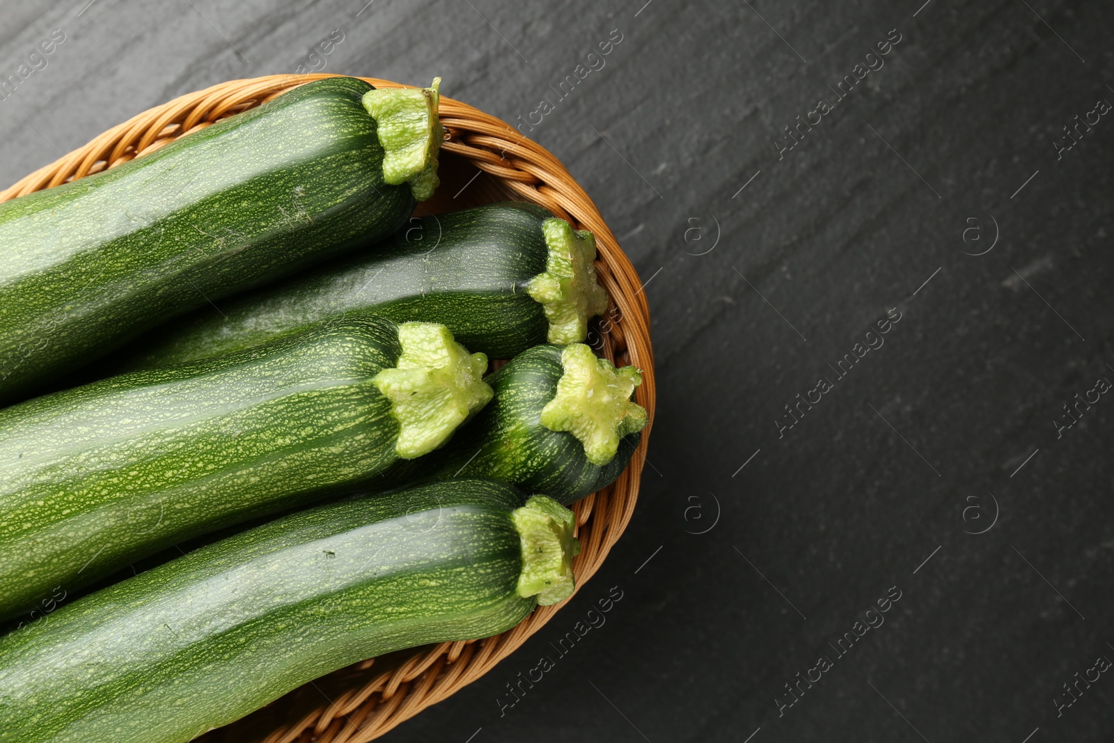 Fresh ripe zucchinis in wicker basket on black table, top view. Space for text Photo of Fresh ripe zucchinis in wicker basket on black table, top view. Space for text