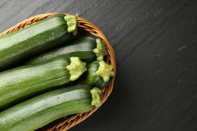 Photo of Fresh ripe zucchinis in wicker basket on black table, top view. Space for text