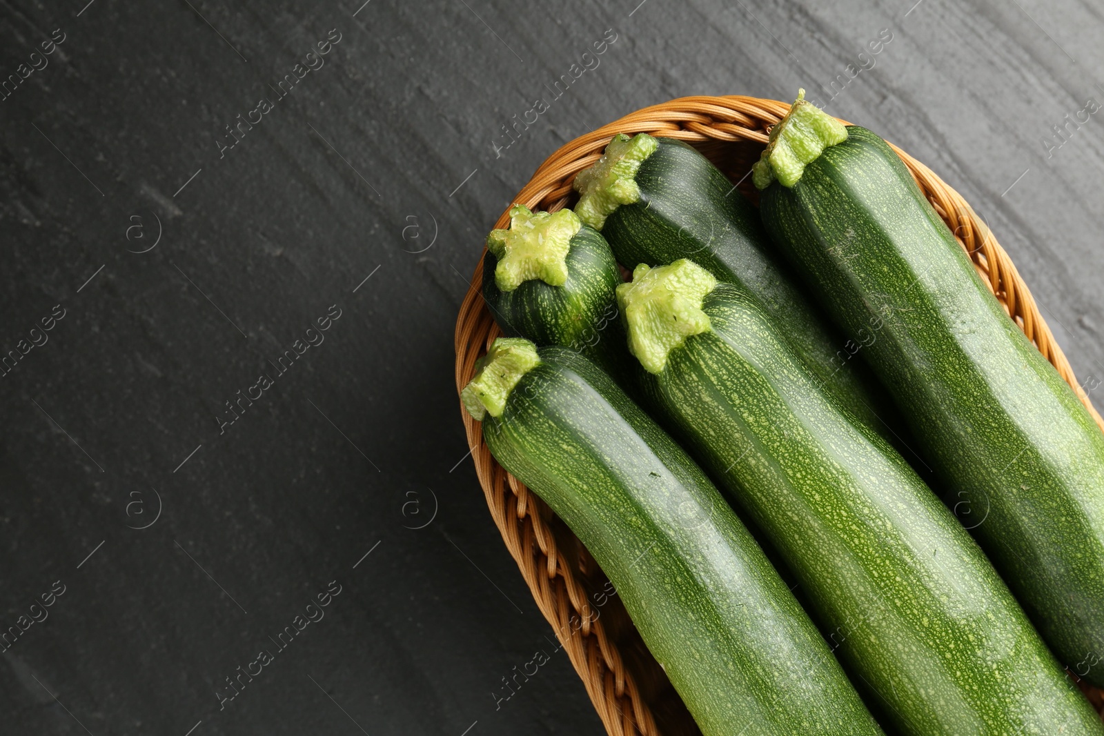 Fresh ripe zucchinis in wicker basket on black table, top view. Space for text Photo of Fresh ripe zucchinis in wicker basket on black table, top view. Space for text