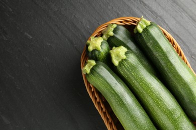 Photo of Fresh ripe zucchinis in wicker basket on black table, top view. Space for text