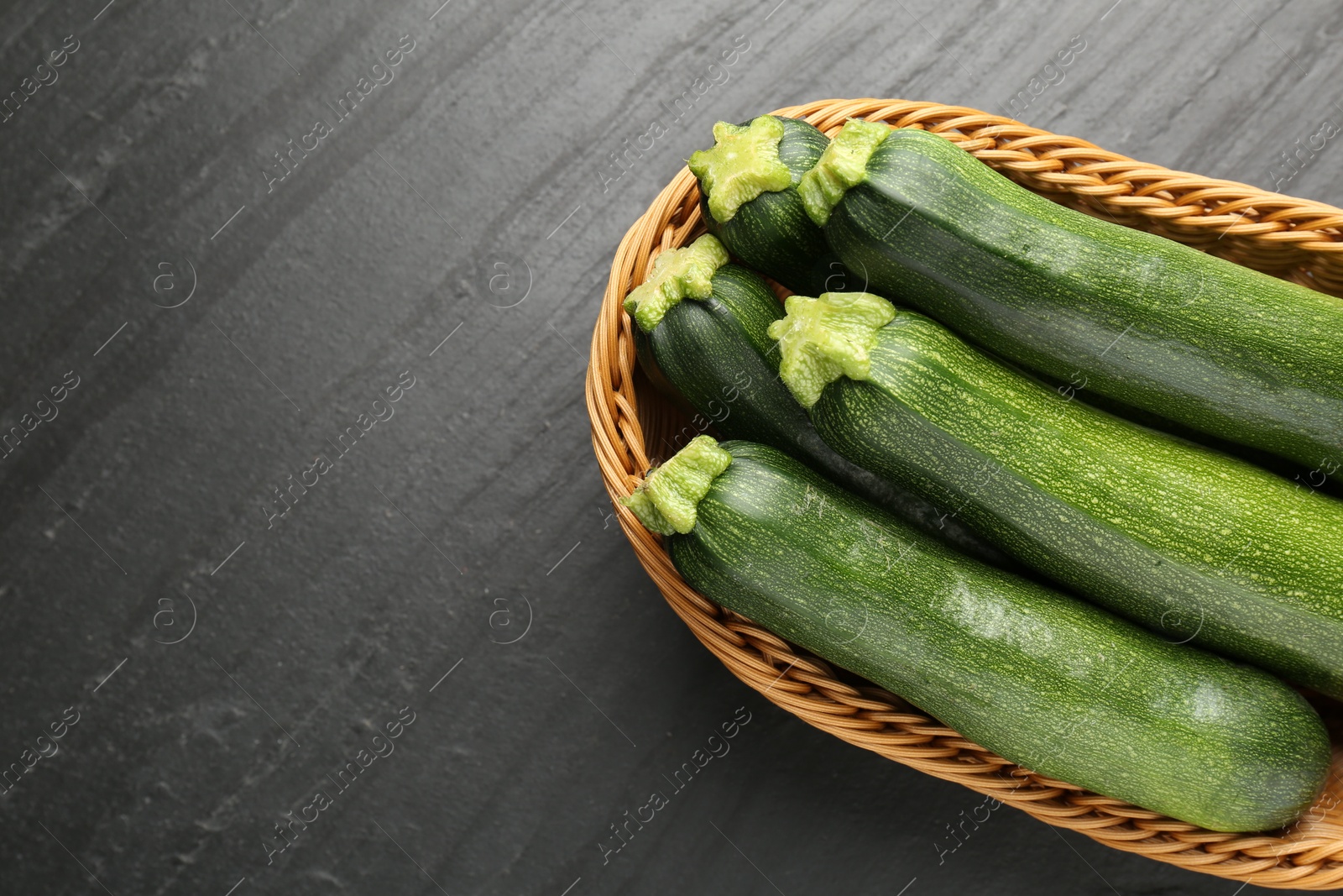 Fresh ripe zucchinis in wicker basket on black table, top view. Space for text Photo of Fresh ripe zucchinis in wicker basket on black table, top view. Space for text