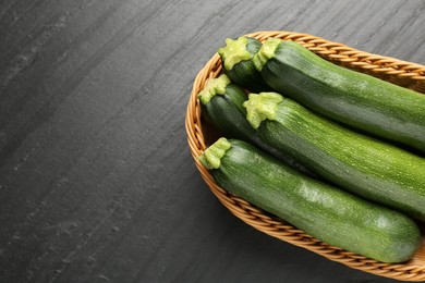 Photo of Fresh ripe zucchinis in wicker basket on black table, top view. Space for text