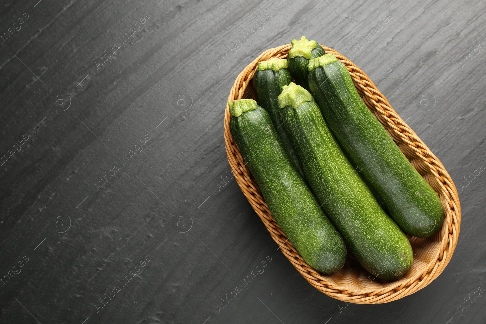 Fresh ripe zucchinis in wicker basket on black table, top view. Space for text Photo of Fresh ripe zucchinis in wicker basket on black table, top view. Space for text