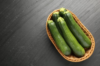 Photo of Fresh ripe zucchinis in wicker basket on black table, top view. Space for text