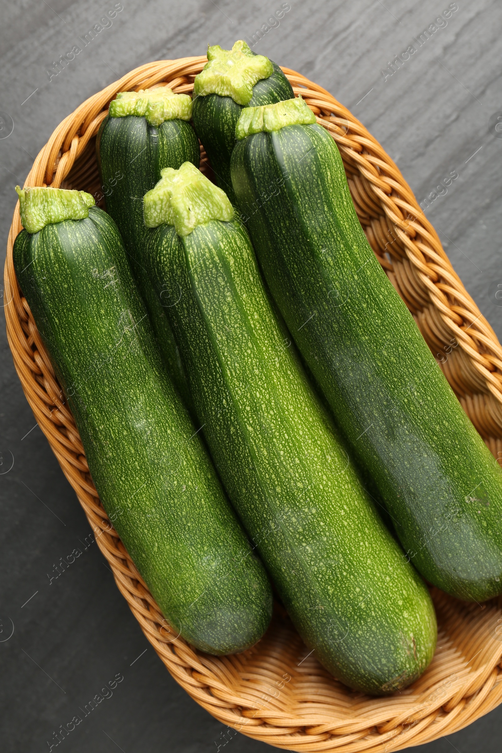 Fresh ripe zucchinis in wicker basket on black table, top view Photo of Fresh ripe zucchinis in wicker basket on black table, top view