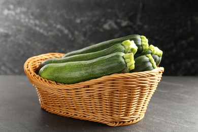 Photo of Fresh ripe zucchinis in wicker basket on black table, closeup