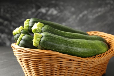 Photo of Fresh ripe zucchinis in wicker basket on black table, closeup