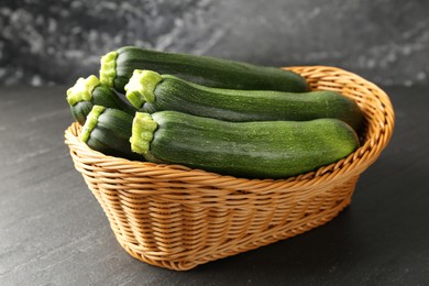 Photo of Fresh ripe zucchinis in wicker basket on black table, closeup