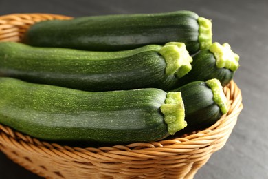 Photo of Fresh ripe zucchinis in wicker basket on black table, closeup