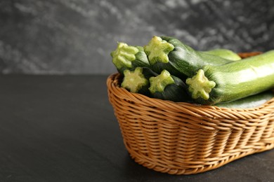 Photo of Fresh ripe zucchinis in wicker basket on black table, closeup. Space for text