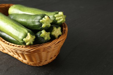 Photo of Fresh ripe zucchinis in wicker basket on black table, closeup. Space for text