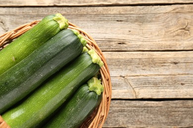 Photo of Fresh ripe zucchinis in wicker basket on wooden table, top view. Space for text