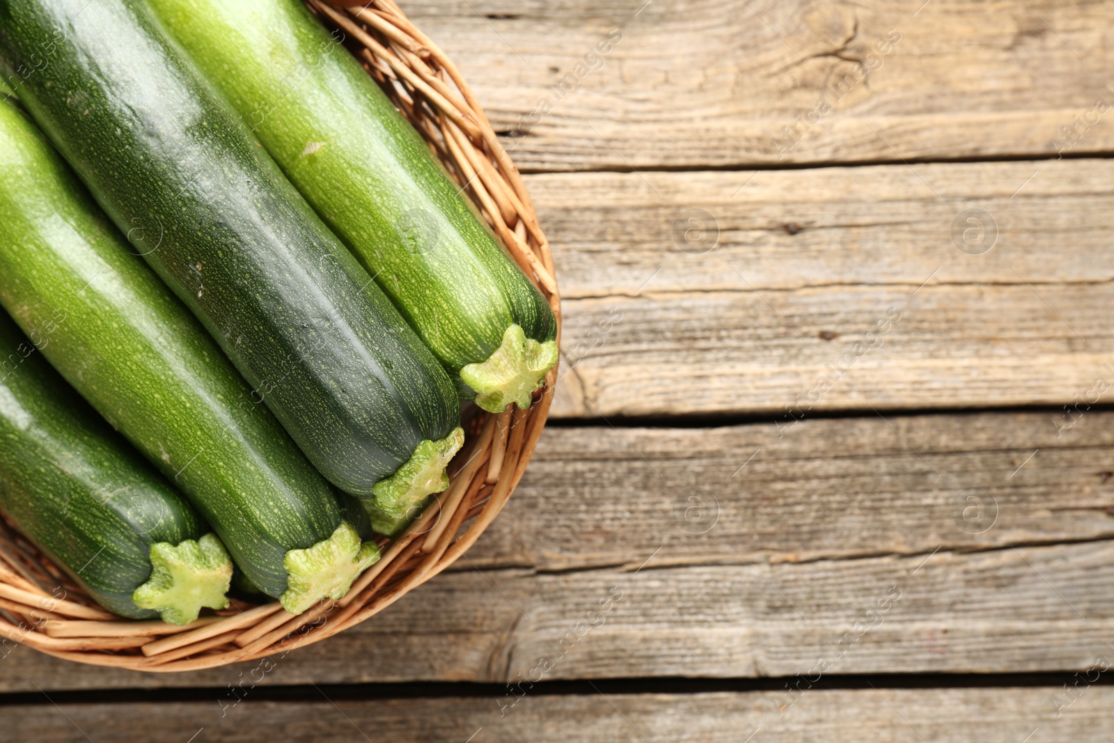 Fresh ripe zucchinis in wicker basket on wooden table, top view. Space for text Photo of Fresh ripe zucchinis in wicker basket on wooden table, top view. Space for text