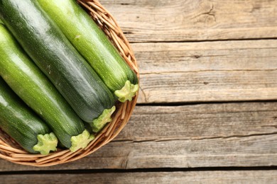 Photo of Fresh ripe zucchinis in wicker basket on wooden table, top view. Space for text