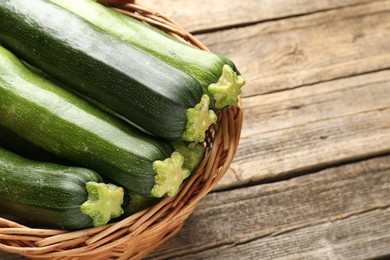 Photo of Fresh ripe zucchinis in wicker basket on wooden table, closeup. Space for text