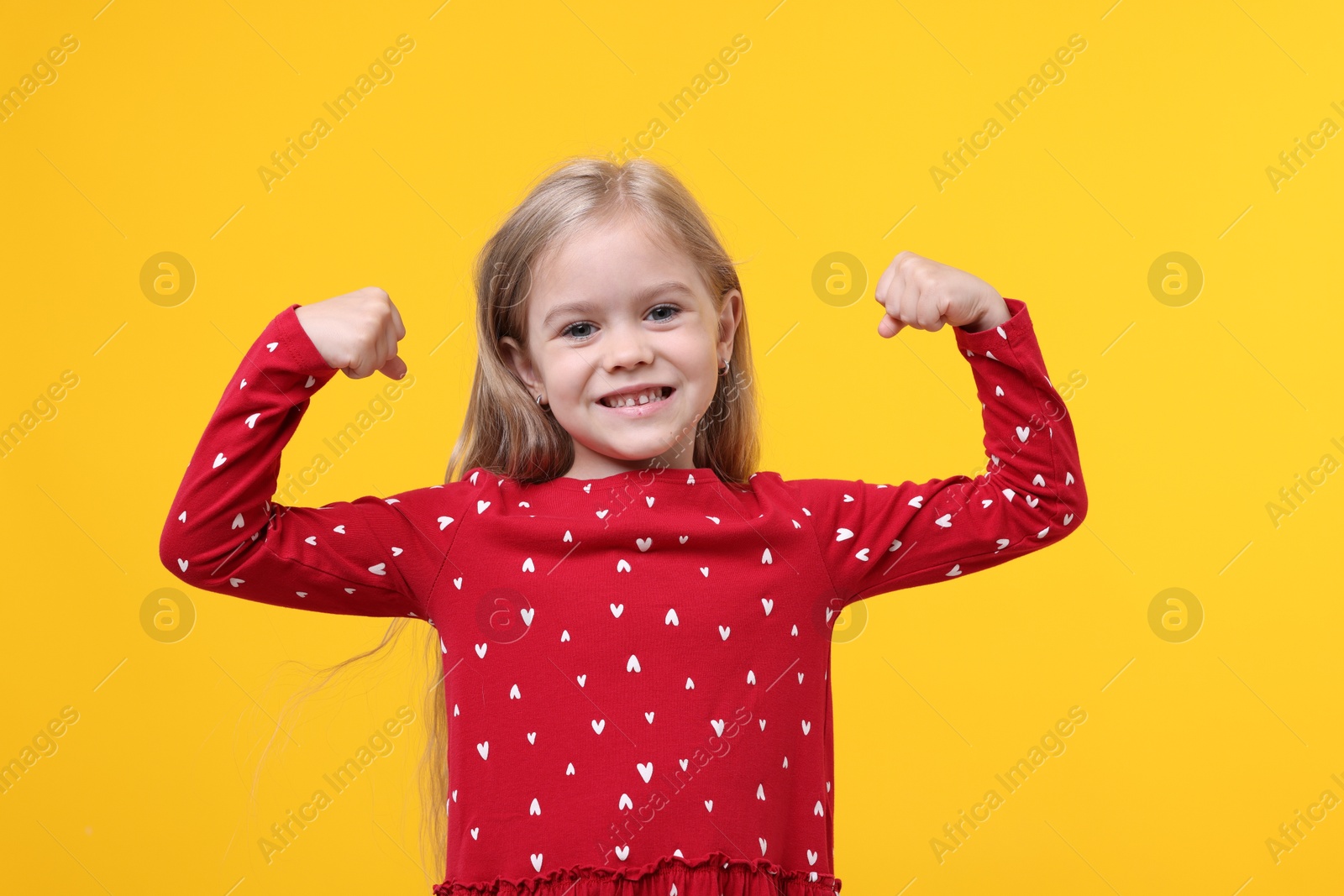 Strength. Happy little girl showing her biceps on yellow background Photo of Strength. Happy little girl showing her biceps on yellow background