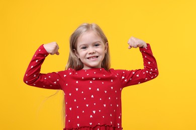 Photo of Strength. Happy little girl showing her biceps on yellow background