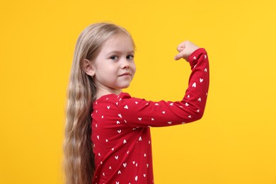 Photo of Strength. Happy little girl showing her biceps on yellow background