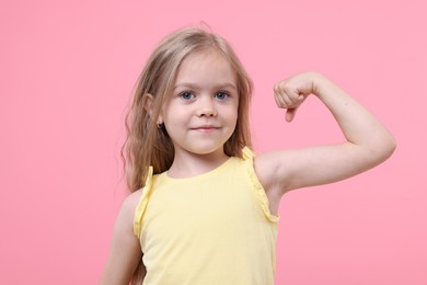 Photo of Strength. Happy little girl showing her biceps on pink background