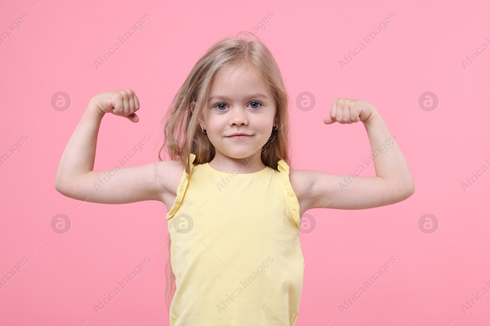 Strength. Happy little girl showing her biceps on pink background Photo of Strength. Happy little girl showing her biceps on pink background