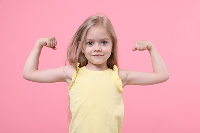 Photo of Strength. Happy little girl showing her biceps on pink background
