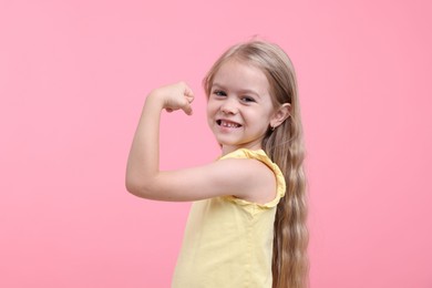 Photo of Strength. Happy little girl showing her biceps on pink background