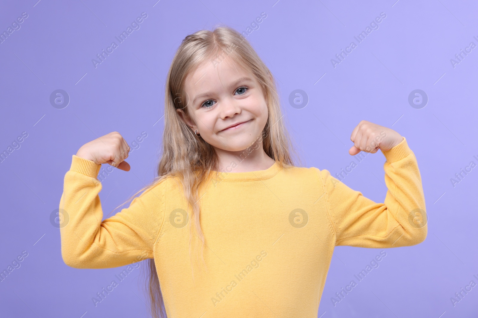 Strength. Happy little girl showing her biceps on purple background Photo of Strength. Happy little girl showing her biceps on purple background