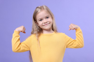 Photo of Strength. Happy little girl showing her biceps on purple background