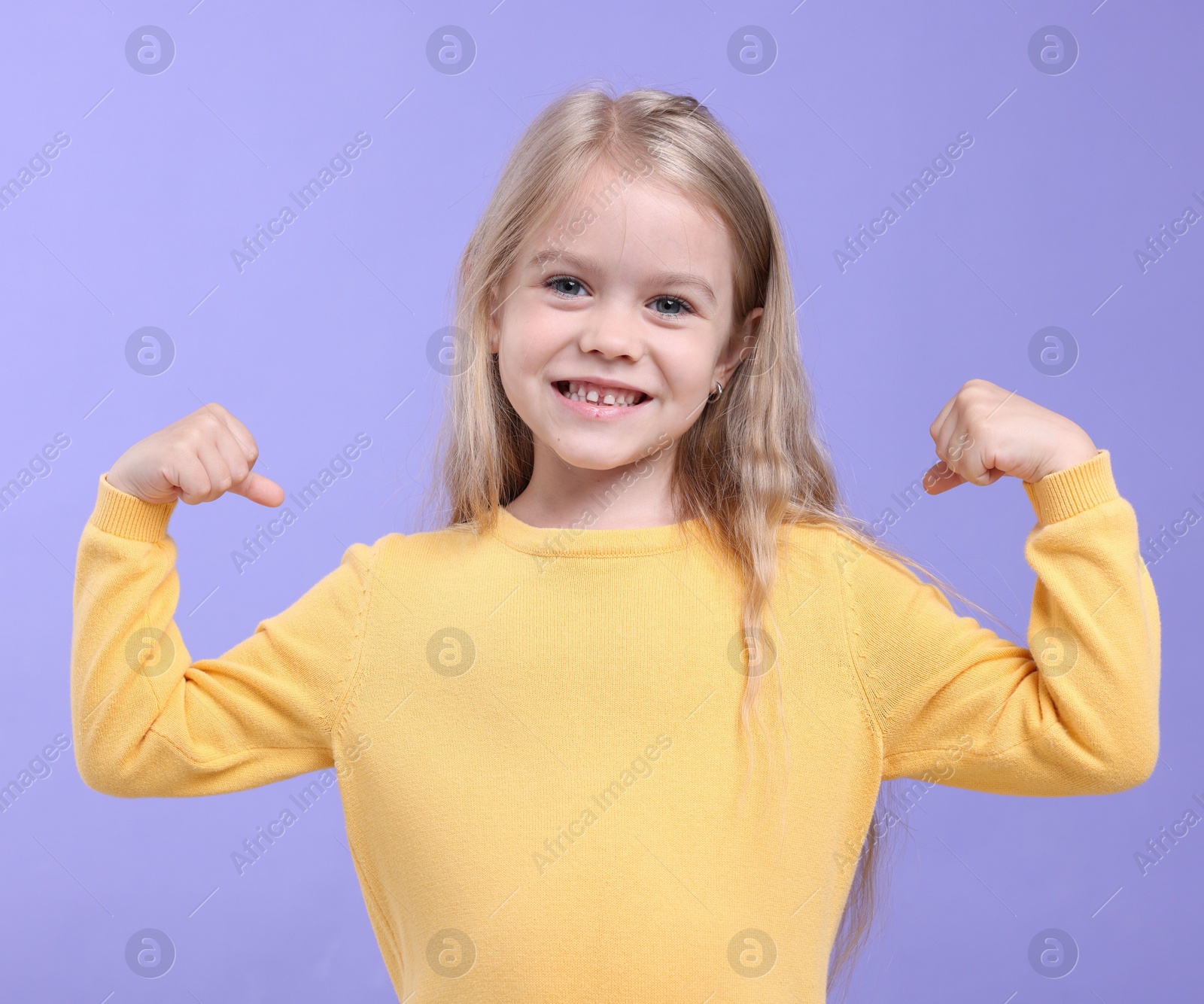Strength. Happy little girl showing her biceps on purple background Photo of Strength. Happy little girl showing her biceps on purple background