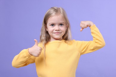 Photo of Strength. Happy little girl showing her biceps and thumbs up on purple background