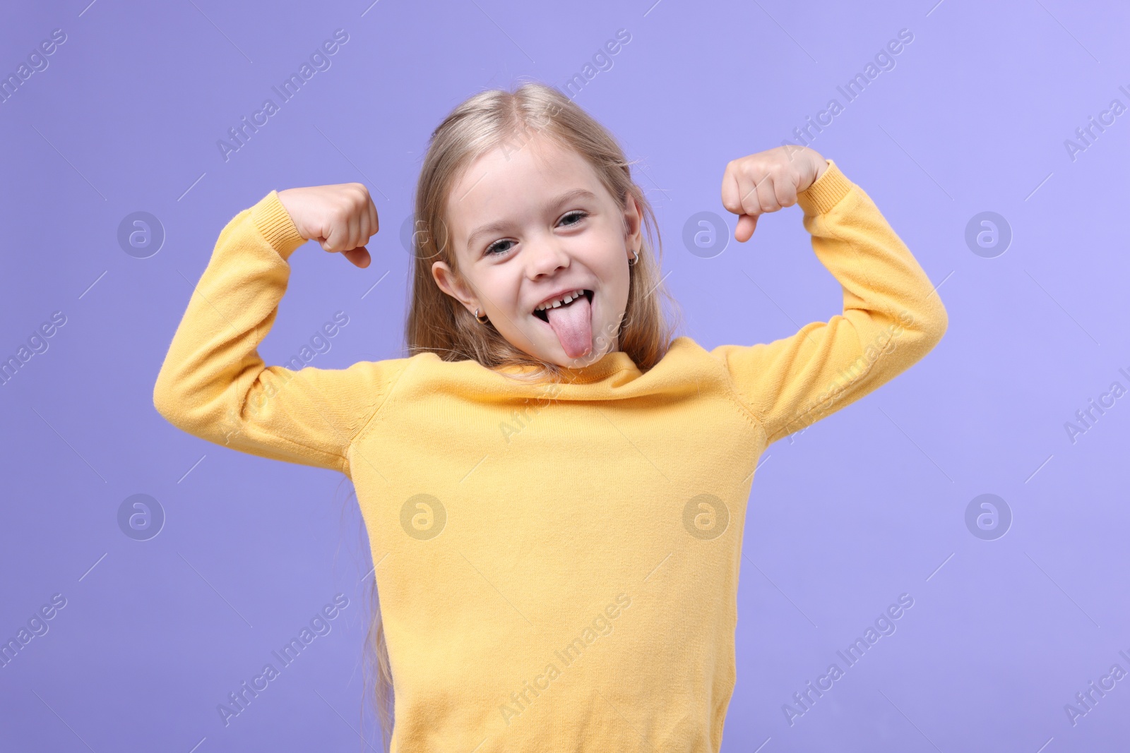 Strength. Happy little girl showing her biceps and tongue on purple background Photo of Strength. Happy little girl showing her biceps and tongue on purple background
