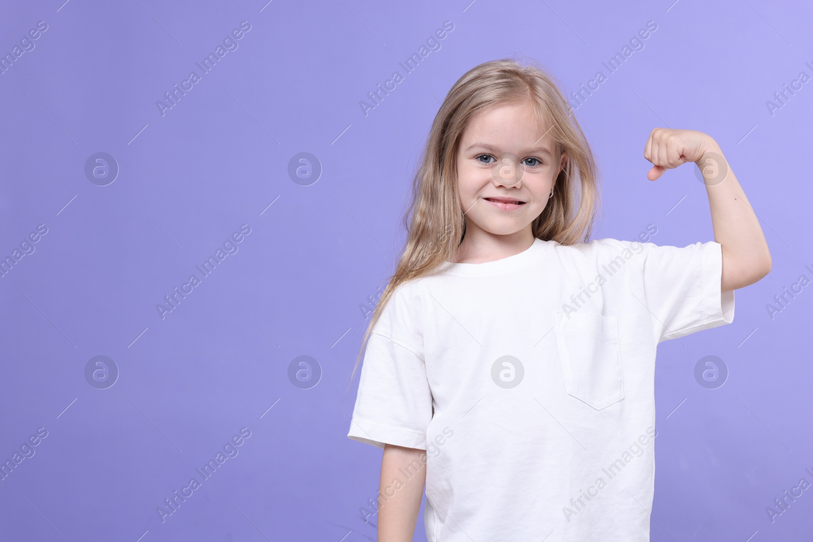 Strength. Happy little girl showing her biceps on purple background, space for text Photo of Strength. Happy little girl showing her biceps on purple background, space for text