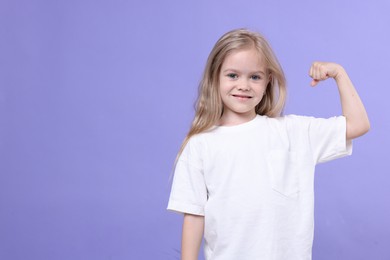 Photo of Strength. Happy little girl showing her biceps on purple background, space for text