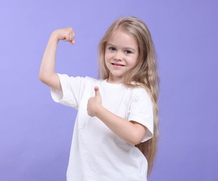 Photo of Strength. Happy little girl showing her biceps and thumbs up on purple background