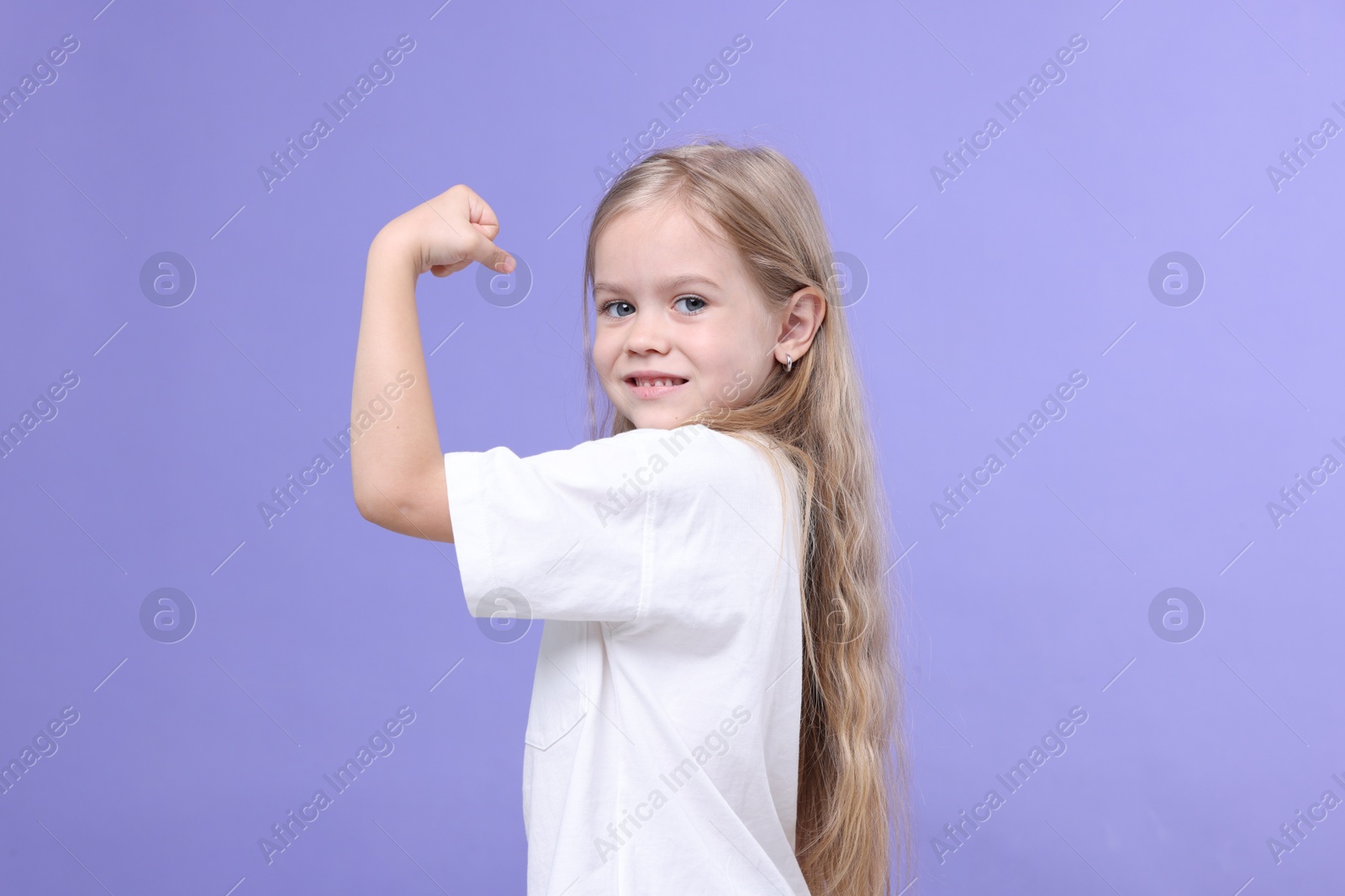 Strength. Happy little girl showing her biceps on purple background Photo of Strength. Happy little girl showing her biceps on purple background
