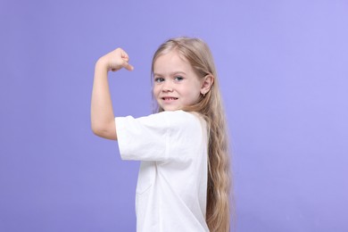 Photo of Strength. Happy little girl showing her biceps on purple background