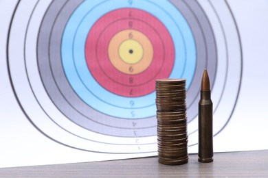 Photo of Firearm cartridge, stack of coins on table against target