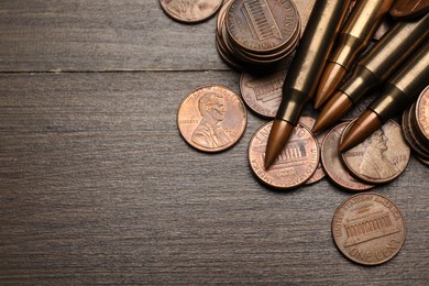 Photo of Firearm cartridges and coins on wooden table, flat lay. Space for text