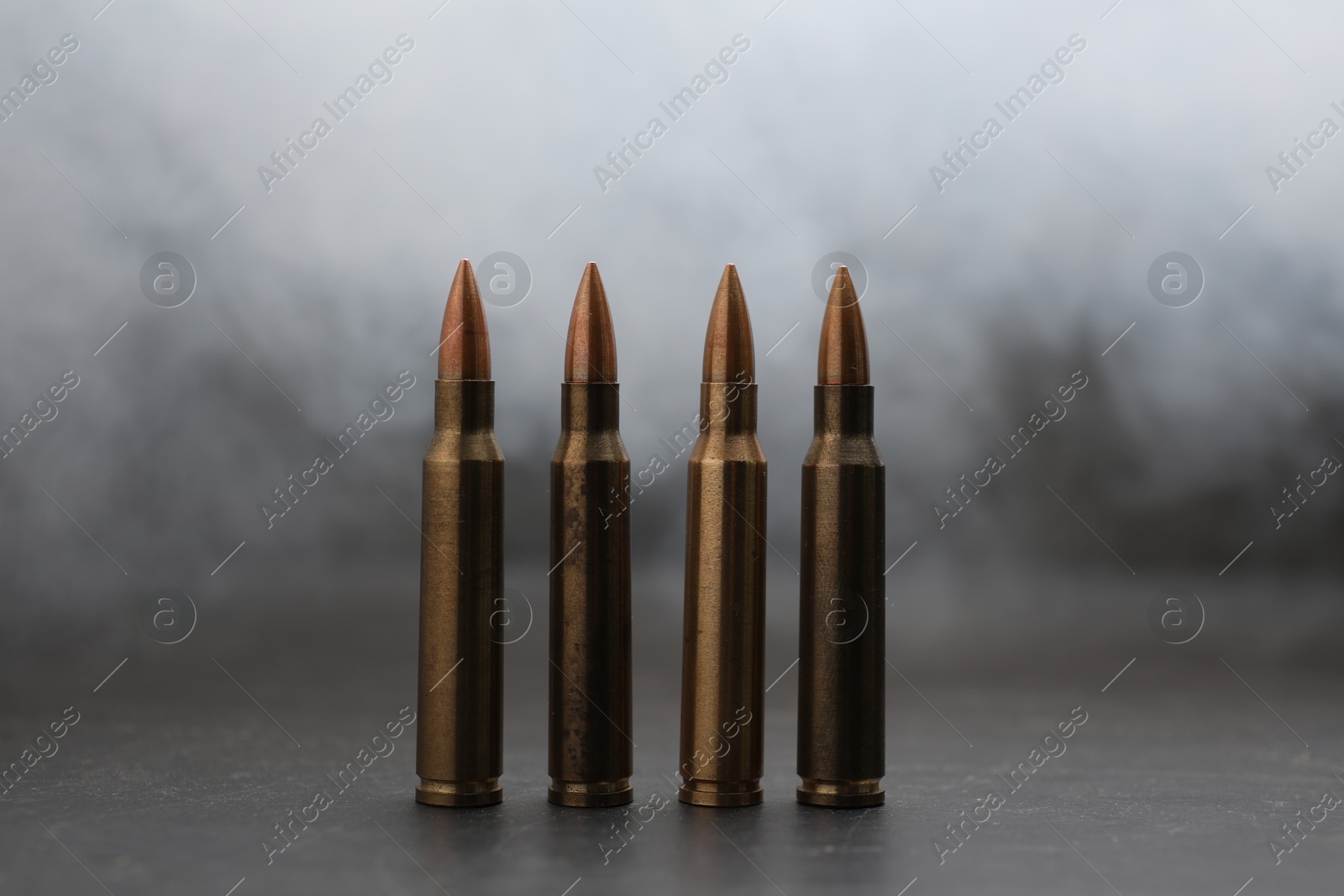 Firearm cartridges on grey table against smoke, closeup Photo of Firearm cartridges on grey table against smoke, closeup