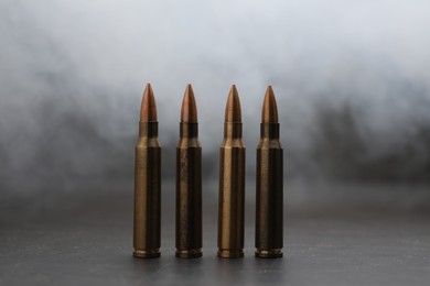 Photo of Firearm cartridges on grey table against smoke, closeup